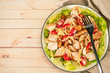 Exquisite variation of Caesar salad with small bites of chicken, cherry tomatoes and a gourmet aioli sauce in a small bowl on a rustic table. Top view. Copy space. Natural and healty food.