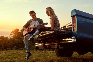 Plakat Love and leisure in perfect harmony. Shot of a young man playing guitar for his girlfriend on a roadtrip.