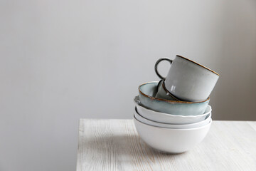 A pyramid of white bowls, plates and cups of different sizes and colors on a beige table in the kitchen. Scandinavian style. Place for your text. Copy space