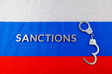 the word sanctions laid with silver metal letters on russian tricolor flag near handcuffs in...