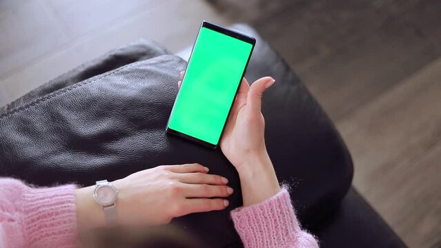 Use green screen for copy space closeup. Chroma key mock-up on smartphone in hand. Woman holds mobile phone iPhone and swipes photos or pictures left indoors of cozy home.