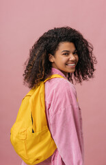 Beautiful smiling African American student with backpack looking at camera isolated on pink background. Back to school, education concept