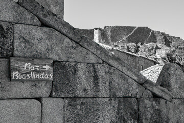 Grayscale shot of an old brick wall with a sign of a bar's direction