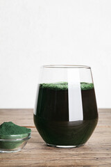 fresh green drink with spirulina in glass, spirulina powder with spoon on wooden background. useful habits, self care and healthy lifestyle.copy space