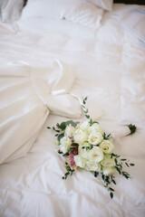 Wedding dress hanging in the room. Scenery for the morning of the bride with a white wedding dress and a bouquet.