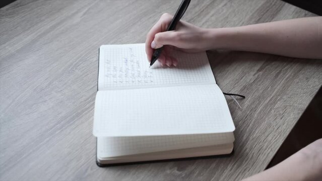 A woman hand writes her wish list with a pen in a notebook. Letter and notes. High quality FullHD footage