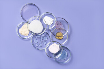 Cosmetic products, scrub, face serum and gel in many petri dishes on a violet background. Cosmetics...