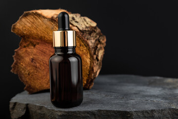 Brown bottle with dropper with a beauty serum tree species on black background. Glass packaging for...