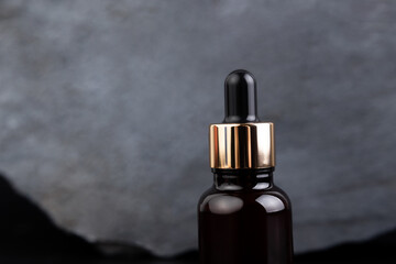Brown bottle with dropper with a beauty serum granite stone on black background. Glass packaging for cosmetic product, essential aroma oil. Skin care, hydration and nutrition with collagen.
