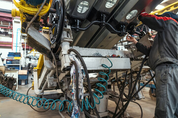 Workers at farm machinery factory assemble spare parts on special machine tool in workplace.