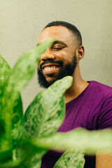 bright close portrait of a smiling black male gardener holding his large green plant 