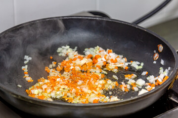 The cook is frying onions and carrots cut into thin slices in a frying pan