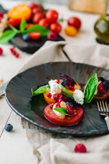 Mix of tomatoes with ricotta cheese, basil, berries and roasted hazelnuts. Restaurant summer dish on a black plate