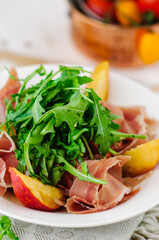 Salad bowl with grilled peach, prosciutto, goat cheese, walnuts and arugula on white background, top view, copy space