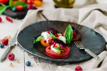 Mix of tomatoes with ricotta cheese, basil, berries and roasted hazelnuts. Restaurant summer dish on a black plate