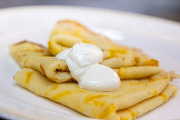Traditional Russian pancakes folded in a triangle with sour cream are on a plate