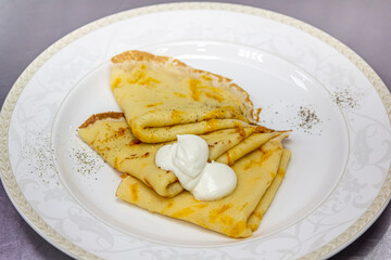 Traditional Russian pancakes folded in a triangle with sour cream are on a plate
