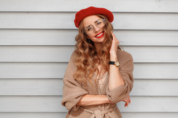 French clothing style, street fashion. A beautiful girl in a cardigan, red beret, and glasses walks through the old city and sits in a cafe. Spring mood and vibes