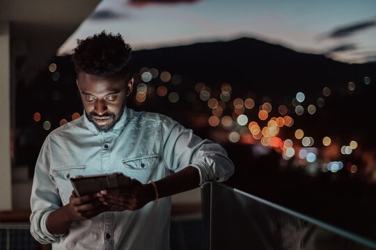 The young man on an urban city street at night texting on smartphone with bokeh and neon city lights in the background. 