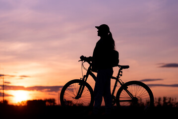 Fototapeta na wymiar Bicycle rider silhouette with sunset sky in background, girl riding her bike staring at the sunny evening sky