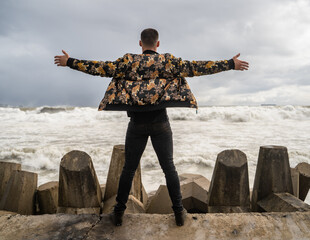 Rear view of a young male in a tiger print jacket standing on the beach with hands outstretched