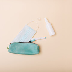 Blue pencil case with face mask on beige background. Minimal concept, top view.