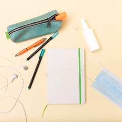 Blue pencil case and white notebook and face mask on pastel pink background. Minimalistic school table concept. Top view.