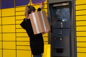 Beautiful woman picking up a package from a smart electronic steel parcel locker box, automatic...
