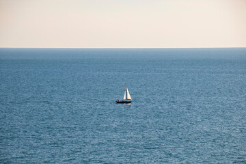 Little white boat in the middle of the blue sea with the horizon and blue sky