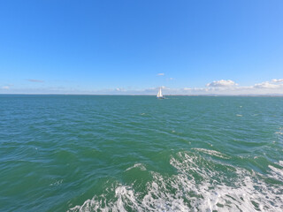 Little white boat in the middle of the blue sea with the horizon and blue sky
