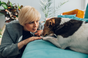 Woman cuddling and playing with her dog at home on the couch