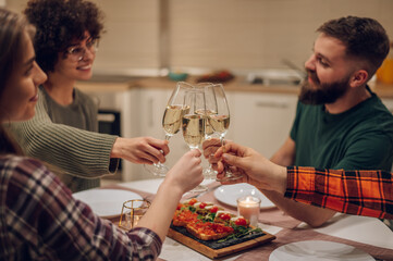 Friends sitting at a kitchen table and toasting during a dinner part