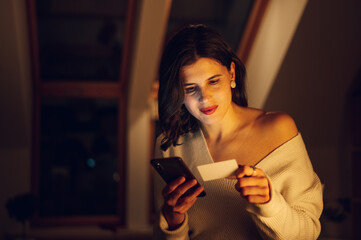 Woman using a smartphone and a credit while relaxing at home in the night