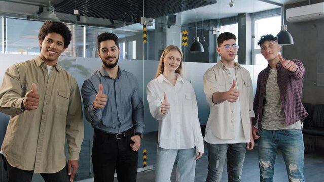 Happy professional confident group diverse people corporate employees standing in row looking at camera smiling showing thumbs up best appreciation gesture approval agreement sign great recommendation