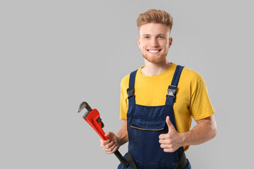 Handsome plumber showing thumb-up on grey background