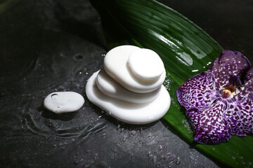 Spa stones with orchid flower and water on dark background