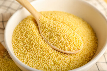 Bowl and spoon with raw couscous on table, closeup