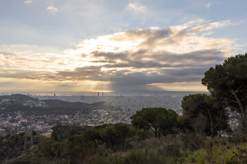 Picturesque landscape of Barcelona from the hill in the early morning. Sunbeams through the clouds. Dramatic sky over the city. Autumn in Barcelona, Spain.