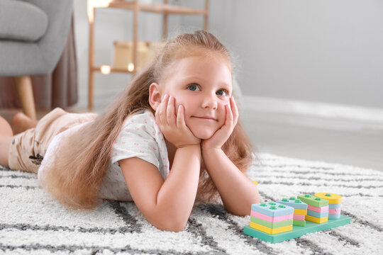 Cute little girl with building blocks lying on floor at home