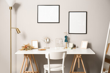 Stylish jewelry on table and blank photo frames on light wall in room
