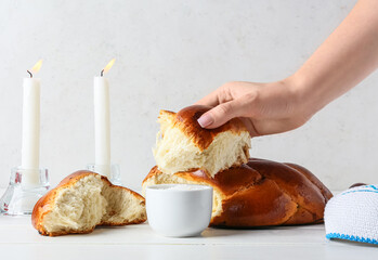Female hand with fresh challah bread and salt in bowl on table