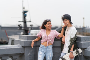 Girl stroking the face of a friend while carrying a skateboard in the port