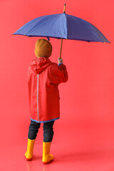 Little boy in raincoat and with umbrella on color background, back view