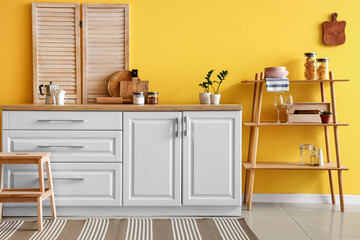 Modern shelving unit with dishware and counter near yellow wall in kitchen