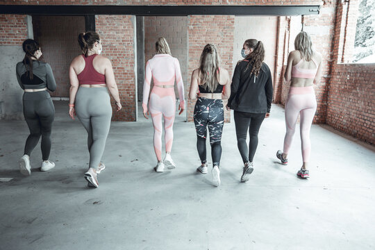 Group of fit female friends of diverse body types in sportswear wearing face masks to protect walking away together after a workout class in a gym. High quality photo