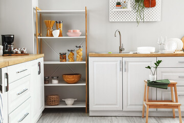 Modern shelving unit with dishware and counters near light wall in kitchen
