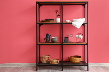 Modern shelving unit with dishware and houseplant near pink wall in kitchen