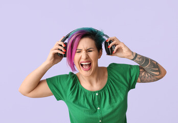 Beautiful woman with unusual hair and tattoo listening to music on color background