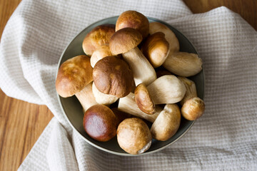 Bunch of fresh wild porcini mushrooms in a round bowl on a wooden oak board, top view