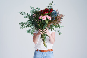 Flowers for someone you love. Studio shot of an unrecognizable woman covering her face with flowers against a grey background.